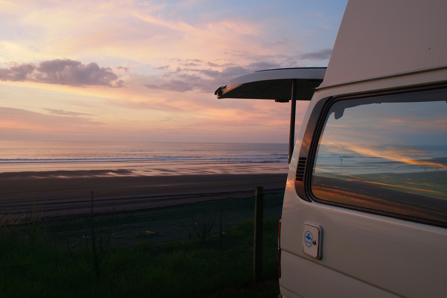 Un van aménagé garé face à une plage au coucher du soleil